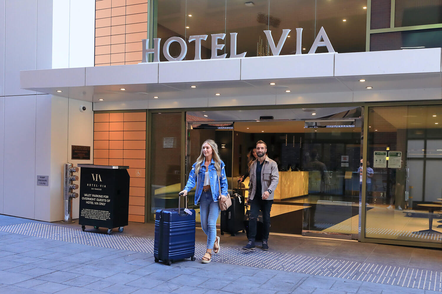 Two people standing outside of a [hotel near Chase Center] with luggage.